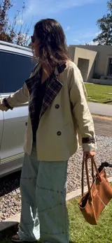 Campera tipo trench corta de gabardina color beige, con diseño de doble botonadura y solapas con forro interior a cuadros. Presenta mangas largas con puños ajustables y corte holgado.