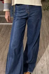 Pantalón de jean azul oscuro con corte wide leg, tiro alto y costuras verticales decorativas en el frente. Presenta un ruedo desflecado y un diseño de pierna ancha.