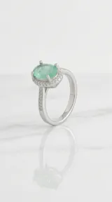 Anillo de plata 925 con piedra central ovalada de color verde claro, rodeada por un halo de pequeñas piedras brillantes y banda decorada con cristales.