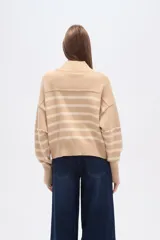 Sweater de punto color beige con rayas horizontales color crema, cuello alto y corte holgado. Presenta costuras decorativas en hombros y pecho.