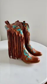 Botas tejanas de cuero color marrón terracota, con detalles pintados a mano en tonos turquesa y negro, diseño con flecos largos y puntera perfilada.