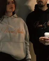 Hoodie color beige con capucha, cordones ajustables y bolsillo tipo canguro. Estampa bordada en el frente con la leyenda "Poona Studio".