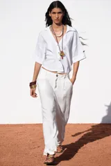 Camisa de lino color celeste claro, con cuello solapa, escote pico, manga corta con vuelta y dos bolsillos de plastrón en el delantero. Cierre frontal con botones.