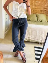 Pantalón de jean tiro alto con caderín ancho regulable mediante cordones frontales. Presenta un diseño de corte recto con terminación en volados en el ruedo.
