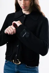 Cardigan de punto acanalado color negro, con cuello camisero, cierre frontal de botones y dos bolsillos delanteros aplicados.