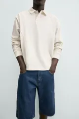 Polo de manga larga color crema, confeccionado en tejido de algodón, con cuello solapa y cierre frontal de botonadura. Presenta un calce relajado y acabados en rib en puños y ruedo.