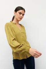 Camisa de manga larga color verde mostaza, con cuello mao, escote en V y botones forrados. Presenta detalles fruncidos en el cuello y puños elastizados.