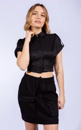 Camisa negra de corte cropped y entallado, con cuello clásico, cierre frontal con botones y mangas cortas.