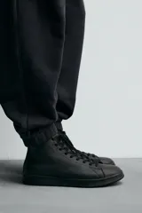 Zapatilla tipo botín de estilo minimalista fabricada en piel lisa de color negro. Presenta un diseño de caña media con cierre de cordones al tono y suela plana de goma a juego.