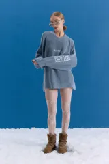 Sweater de tejido de punto grueso en color azul grisáceo, con escote redondo y diseño holgado. Presenta estampado gráfico en el frente y en una de las mangas, con terminaciones acanaladas en cuello, puños y ruedo.