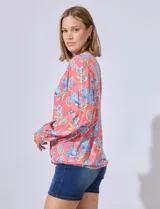 Blusa estampada con cuello a la base, escote en V y aplique de puntilla. Terminación de ruedo con nudo.