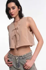 Top corto sin mangas color beige arena, con escote en V y cierre frontal mediante lazos anudados.