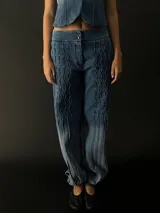 Pantalón babucha de jean con corte a la cintura y piernas amplias y rectas con textura vertical. Presenta elástico y broches inferiores en el puño.