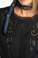 Blusa negra de algodón con corte oversize, mangas cortas abullonadas y detalles de encaje y bordados en el frente y hombros. Presenta un diseño con pliegues verticales y terminaciones con puntilla.