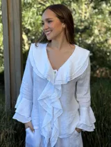 Camisa de lino azul marino con volados en cascada a lo largo del frente y en los puños de las mangas largas. Presenta un escote en V con un botón de nácar visible.