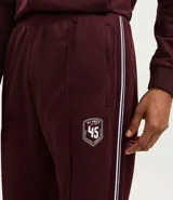 Pantalón deportivo color bordó con rayas blancas laterales, cintura elástica con cordón ajustable, bolsillos laterales y logo pequeño en el muslo.