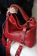 Cartera tipo morral de cuero color rojo intenso, con diseño texturizado trenzado, herrajes metálicos en tono bronce envejecido, manija corta superior y correa regulable desmontable.