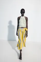 Falda midi tipo pareo de tiro medio, confeccionada en algodón con diseño de rayas verticales en tonos amarillo, gris y blanco. Presenta un bajo asimétrico y cierre lateral con lazada.