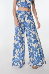 Pantalón ancho de tiro alto, color beige con estampado floral en azul. Presenta pliegues en la cintura y lazo para ajustar.
