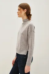Polera de lana y cachemira color gris, con cuello alto y mangas largas con textura acanalada. Presenta un diseño holgado con aberturas laterales en el ruedo.