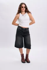 Bermuda de jean negro con efecto acid wash y diseño amplio de corte bermuda, con bolsillos laterales y traseros, y cierre frontal con botón y cremallera.