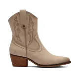 Bota texana de caña media en color beige, con diseño de costuras decorativas y detalles de tachas metálicas. Presenta un taco cuadrado de madera y punta almendrada.