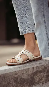 Sandalias planas de cuero negro, con diseño de tiras anchas interconectadas y punta cuadrada, decoradas con tachas metálicas doradas.