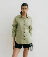 Camisa de lino color verde claro, de manga larga con puños anchos y botones negros frontales. Corte holgado con aberturas laterales.