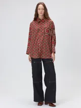 Camisa de seda con estampado geométrico de cuadrados en tonos rojizos y marrones. Presenta cuello camisero, cierre frontal con botones, bolsillo en el pecho y mangas largas con puños abotonados.