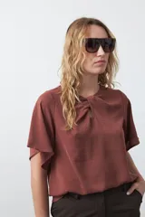 Top negro de manga corta con detalle de nudo en el escote y abertura tipo gota. Presenta una silueta relajada y textura sutil en la tela.