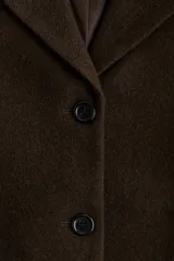 Blazer de botonadura sencilla en tejido afieltrado color marrón oscuro. Presenta solapas de muesca, hombreras, cierre frontal de tres botones y dos bolsillos delanteros de parche. El diseño es forrado y de corte estructurado.