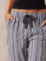 Pantalón de lino con diseño de rayas verticales en tonos grises y blancos. Presenta cintura elástica con lazo de ajuste, bolsillos laterales y corte recto.