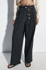 Pantalón de lino negro de tiro medio, con pernera recta, pinzas delanteras y detalle de puntilla en la cintura. Cuenta con bolsillos frontales y cierre con cremallera y botón.