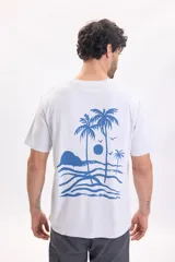 Remera blanca de manga corta con gran estampado azul en la espalda que representa un paisaje tropical con palmeras, mar y aves.