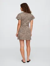 Vestido corto de denim con estampado de leopardo, corte entallado y falda acampanada. Tiene cuello en V, mangas cortas con volados y cierre frontal con botones.