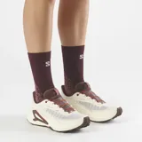 Championes de trail running Salomon Genesis 2, en color beige claro con detalles en bordó y rojo. Cuentan con capellada de Matryx®, sistema de ajuste rápido de cordones Quicklace, suela Contagrip® y tecnología Active Chassis para mayor estabilidad.