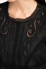 Blusa negra de algodón con diseño de broderie y calados en el pecho y hombros. Presenta corte oversize, mangas largas con puños y un detalle de volado en la cintura.