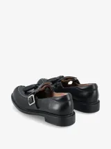 Zapato tipo guillermina o mary jane de cuero negro, con cierre de hebilla lateral, detalle de flecos en el empeine y tachas metálicas decorativas en el borde frontal.