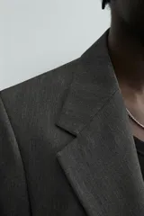 Blazer de corte regular fit en color gris oscuro, confeccionada en tejido con viscosa. Presenta cuello con solapas de muesca, cierre frontal con dos botones, bolsillos laterales con solapa y aberturas en la espalda.