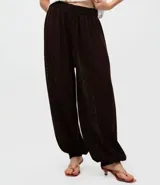 Pantalón de punto estilo aladino, color marrón oscuro, con diseño de tejido calado, cintura elástica y puños ajustados en los tobillos.