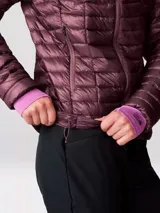 Campera puffer color borgoña con capucha, cierre frontal completo y bolsillos laterales con cierre. Confeccionada con tejido ripstop ultraligero reciclado y relleno de plumón de 800 hilos con certificación RDS.