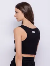 Top blanco de tela texturada, sin mangas y con cuello redondo. Cuenta con cuatro botones y terminación en curva en la parte delantera.