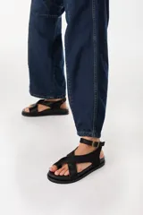 Sandalias planas de cuero color marrón oscuro, con tiras cruzadas en el empeine, sujetadedo y tira ajustable al tobillo con hebilla metálica.