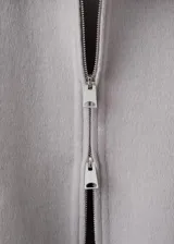 Chaqueta gris de diseño corto y holgado, con cuello alto envolvente, mangas anchas y puños ajustables con tiras y botones. Cuenta con bolsillos laterales y cierre frontal oculto.