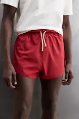 Short de baño rojo de tejido técnico ligero y elástico, con cintura elástica ajustable mediante cordón blanco y aberturas laterales en las perneras.