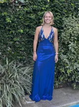 Vestido largo con escote en V, estampado en tonos rojizos y rosados, con un patrón ondulado. Presenta cut-outs laterales bajo el busto y breteles finos que se cruzan en la espalda.