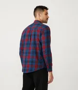 Camisa masculina de franela a cuadros en tonos rojo y azul, de corte comfort, con cuello camisero, manga larga y abotonadura frontal.
