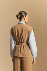 Chaleco negro de corte estructurado con cuello redondo, cierre frontal oculto y lazo ajustable en la cintura. Presenta dos bolsillos frontales con solapa y diseño de hombros caídos.