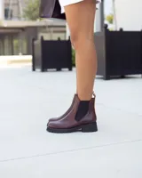 Botas tipo Chelsea de cuero color marrón, con paneles elásticos laterales en color negro y suela de goma dentada en color negro. Presenta un detalle de tirador en la parte trasera en gamuza color tostado.