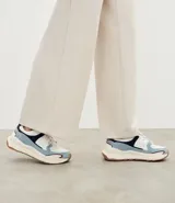 Championes estilo jogging con diseño de recortes contrastantes en tonos blanco, azul y gris. Presenta una parte superior de mesh respirable con sobreposiciones de poliuretano, forro suave y suela robusta de color crema con base marrón.